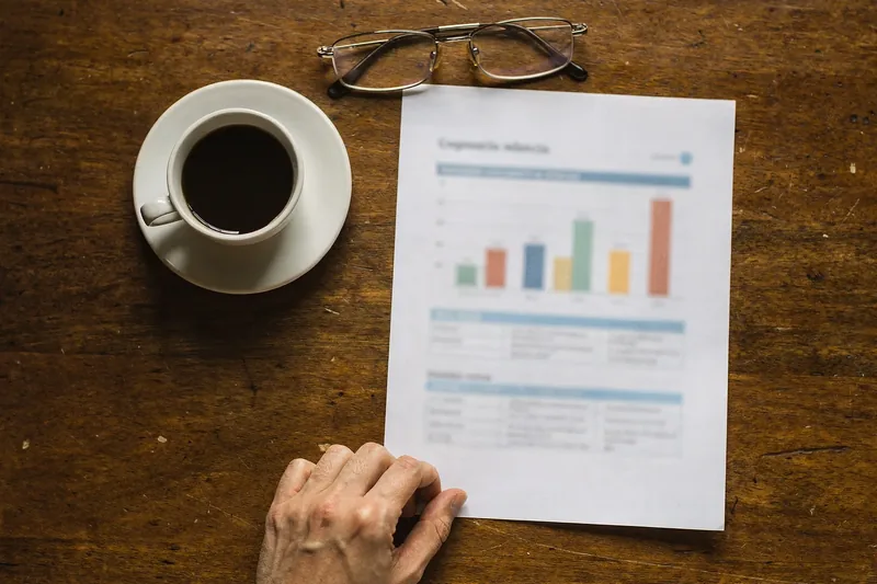 Vista cenital de una mesa con un informe impreso con gráficos de barras, unas gafas y una taza de café