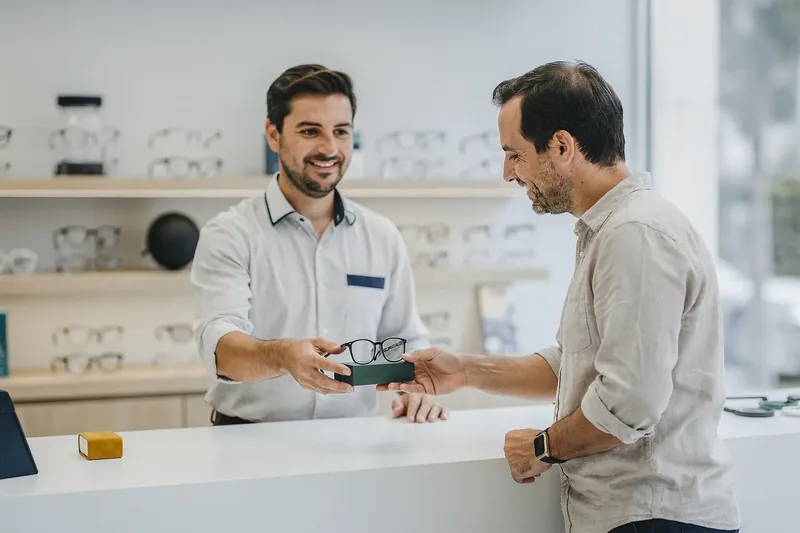 Óptico entregando una funda de gafas a una clienta en el mostrador de la óptica